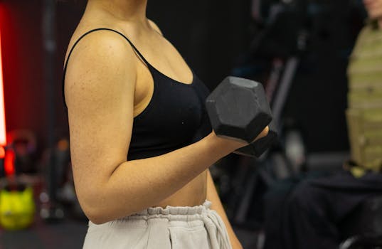 Focused woman lifting a dumbbell in a gym setting, promoting fitness and strength.