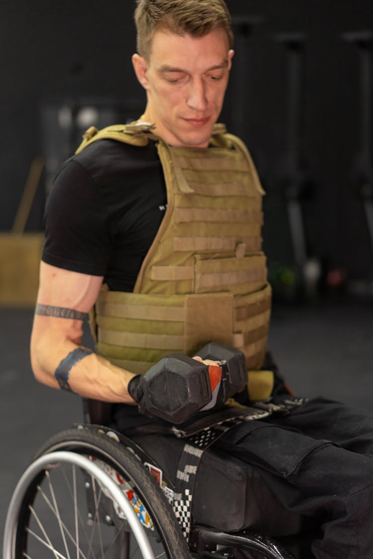 A Man In Black Shirt Sitting On A Wheelchair Lifting A Dumbbell