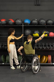 Young woman assists wheelchair-using man during a gym workout, promoting inclusive fitness.