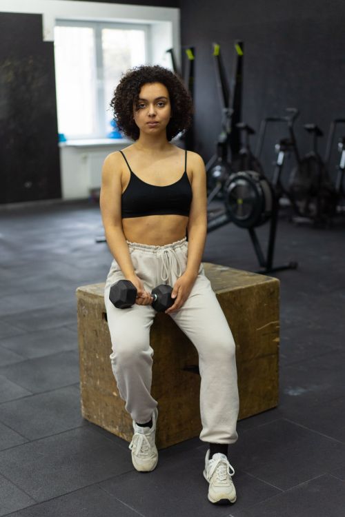 Free Woman with curly hair in activewear holding dumbbells in a contemporary gym setting. Stock Photo