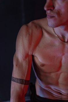 Shirtless muscular man showcasing tattooed arm, captured in dramatic low-lighting for fitness concept.