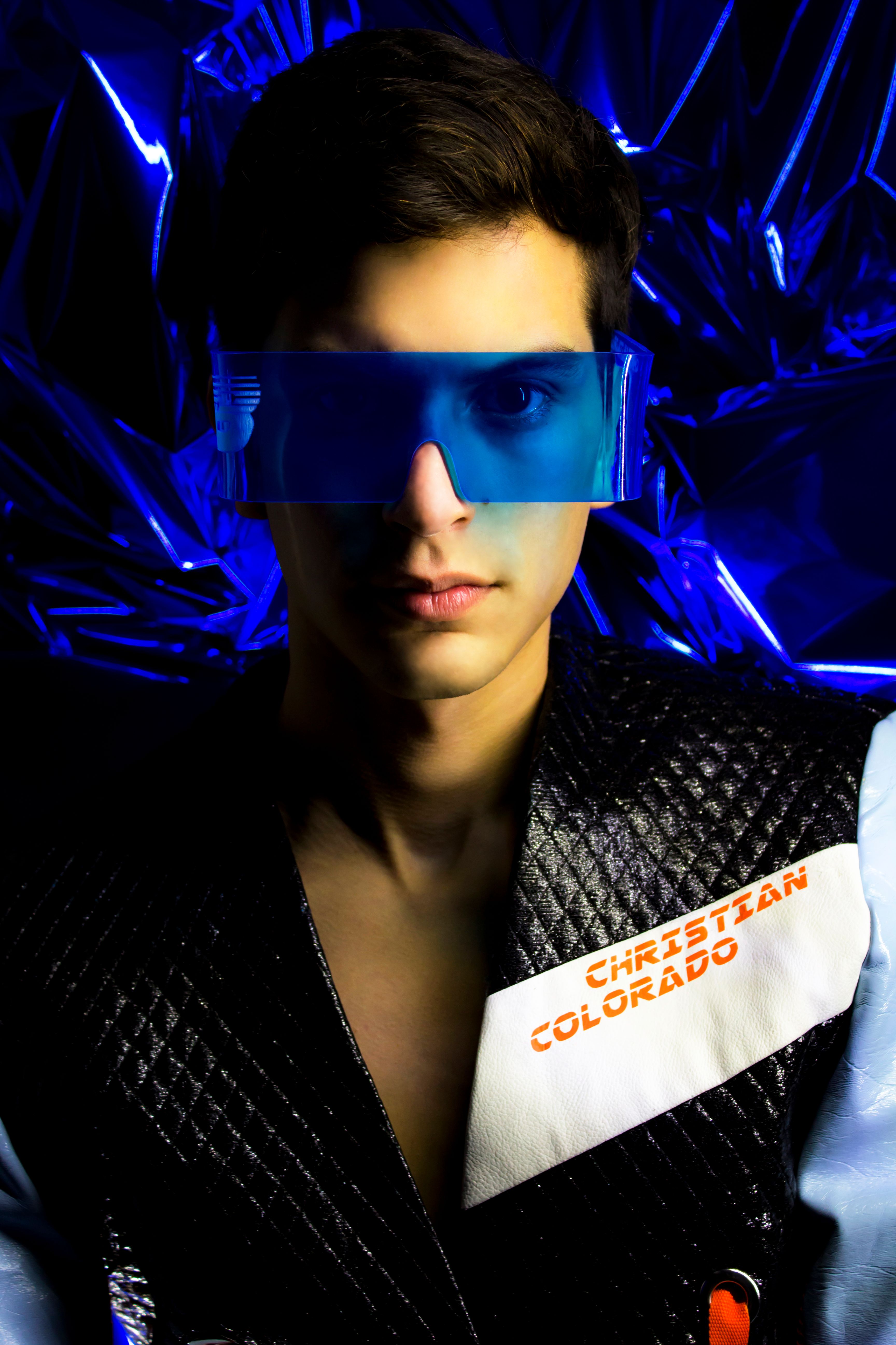 Portrait of a man wearing futuristic blue visor against a metallic backdrop.