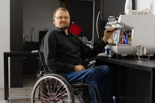 A barista in a wheelchair making coffee with an espresso machine indoors.