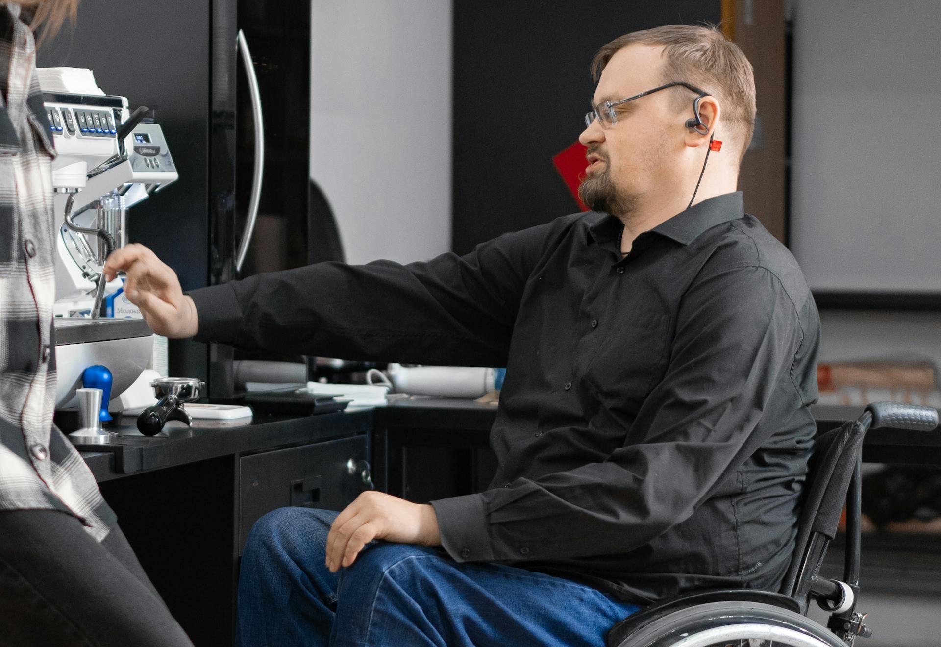 Man in Black Long Sleeve Shirt Sitting on Black Wheelchair in Front of Coffee Machine