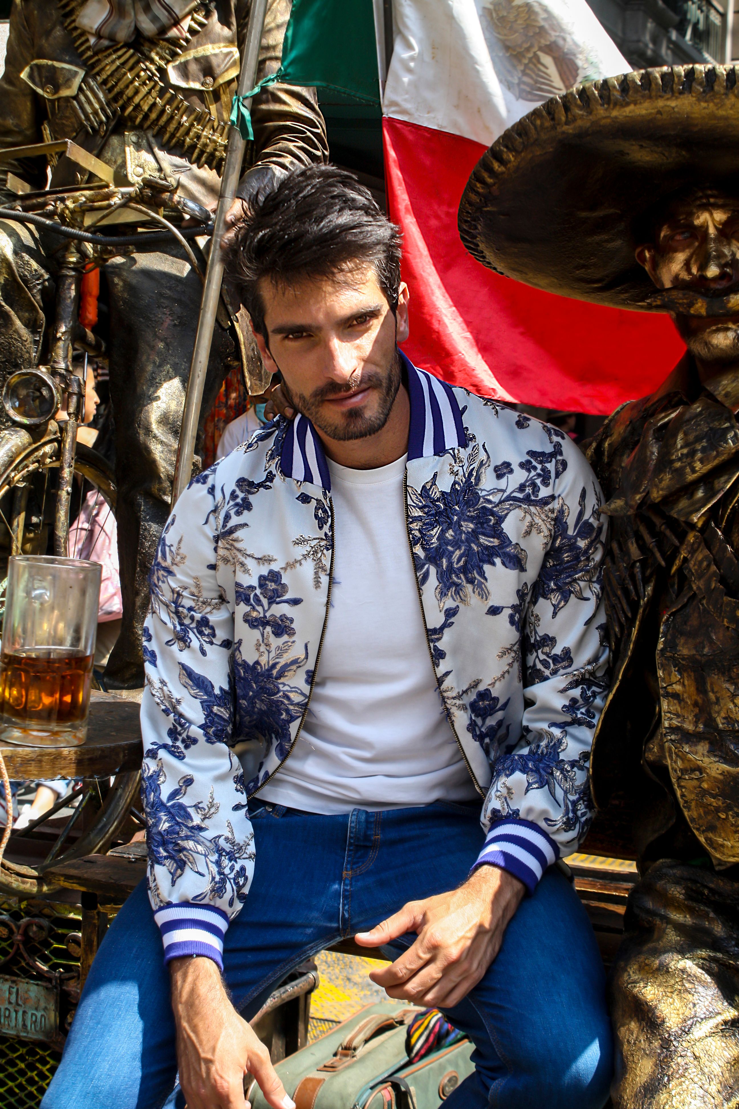 A man in a floral jacket sits beside a sculpture in a vibrant outdoor setting.