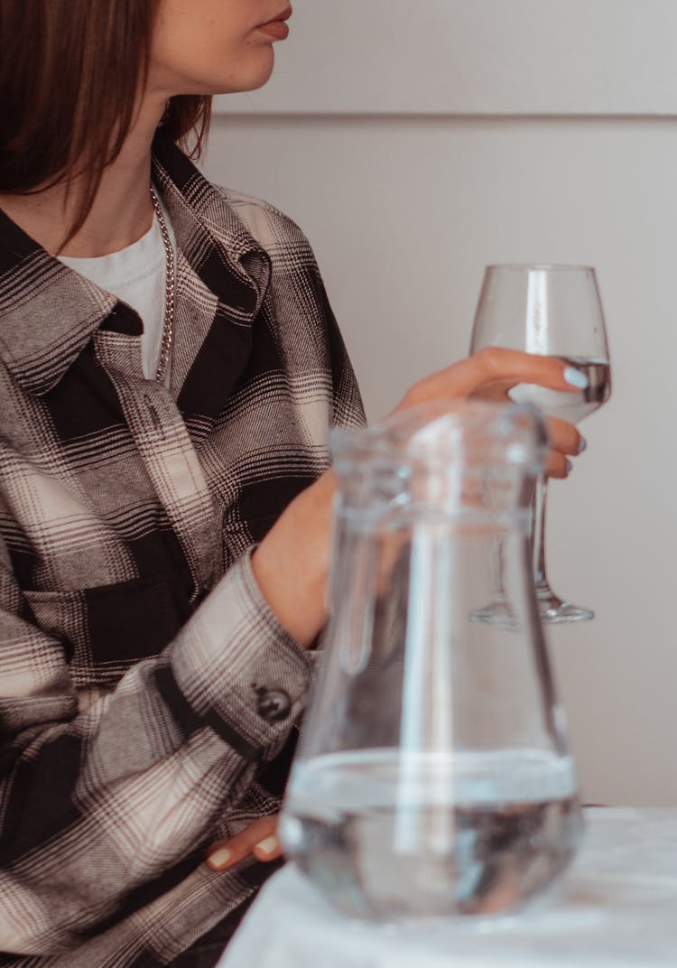 A Person In Plaid Long Sleeves Holding A Goblet Glass With Water