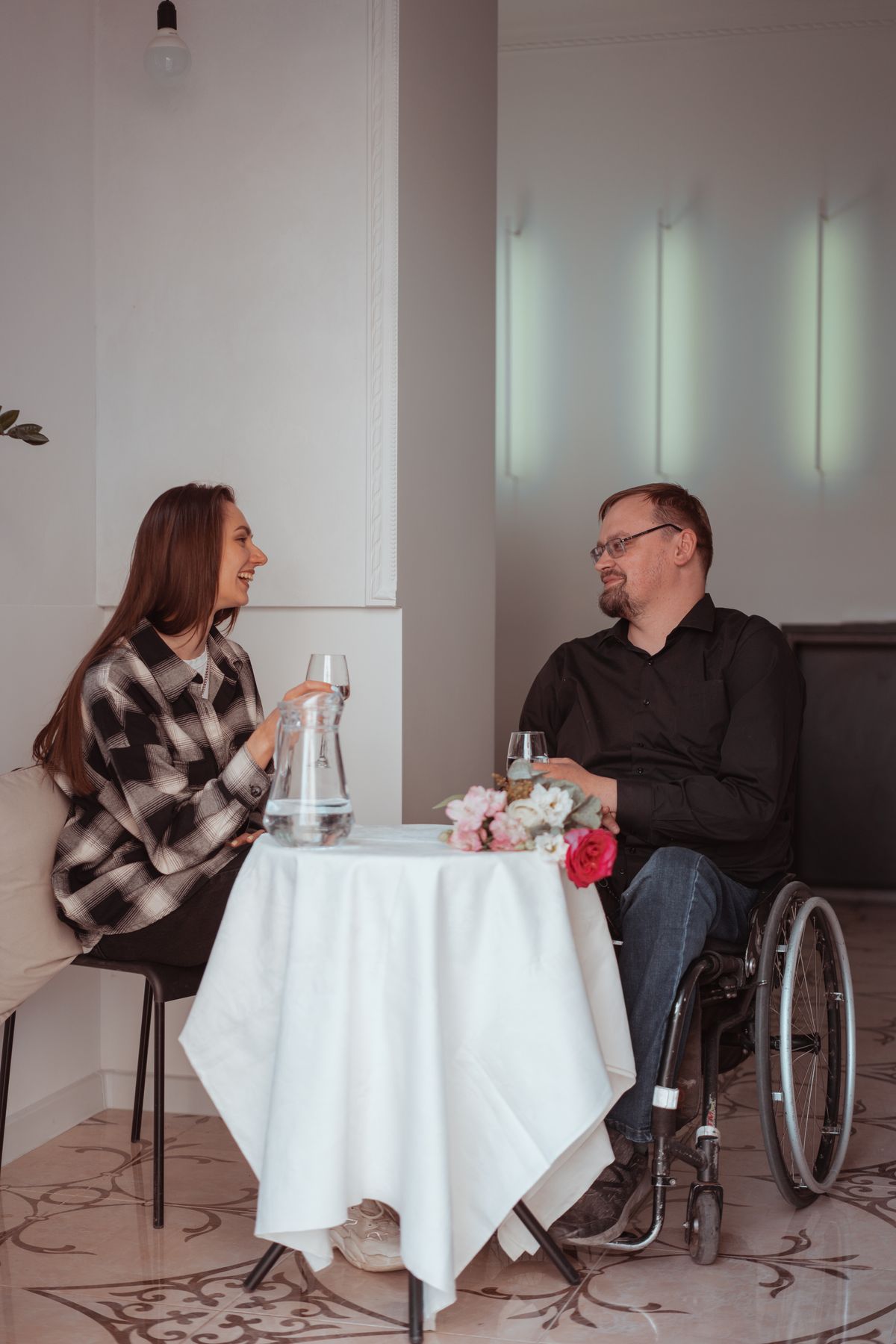 Two people talking at a cafe table, one seated in a wheelchair