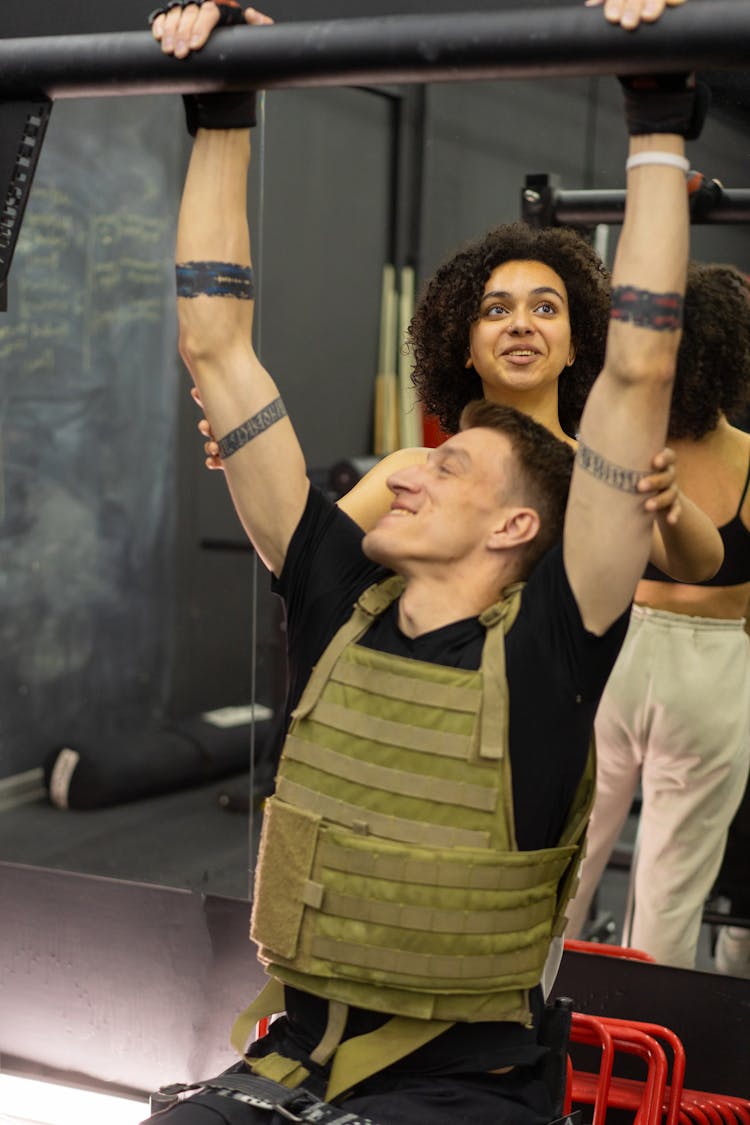 A Woman Supporting A Man In The Pull Up Bar