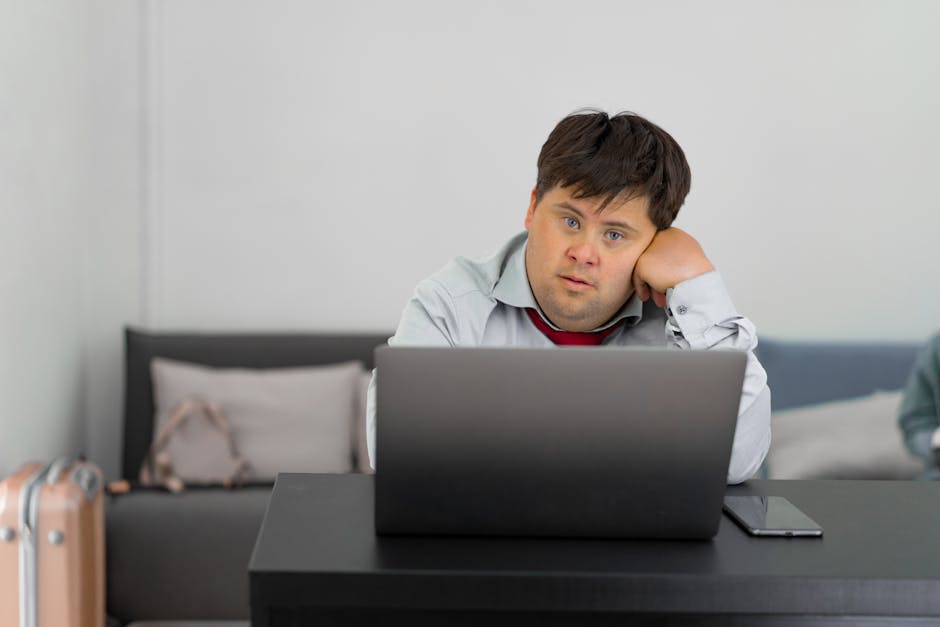 Person with Down Syndrome sitting at a desk, working on a laptop indoors.