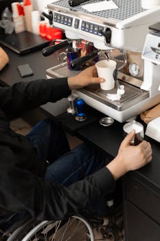 A barista operates an espresso machine to brew coffee in a cafe setting.