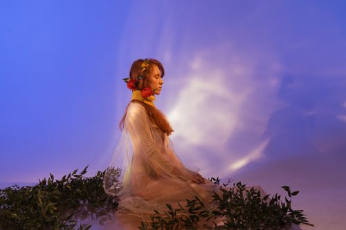 Free Graceful woman in white dress sitting with vibrant flora under colorful lights. Stock Photo