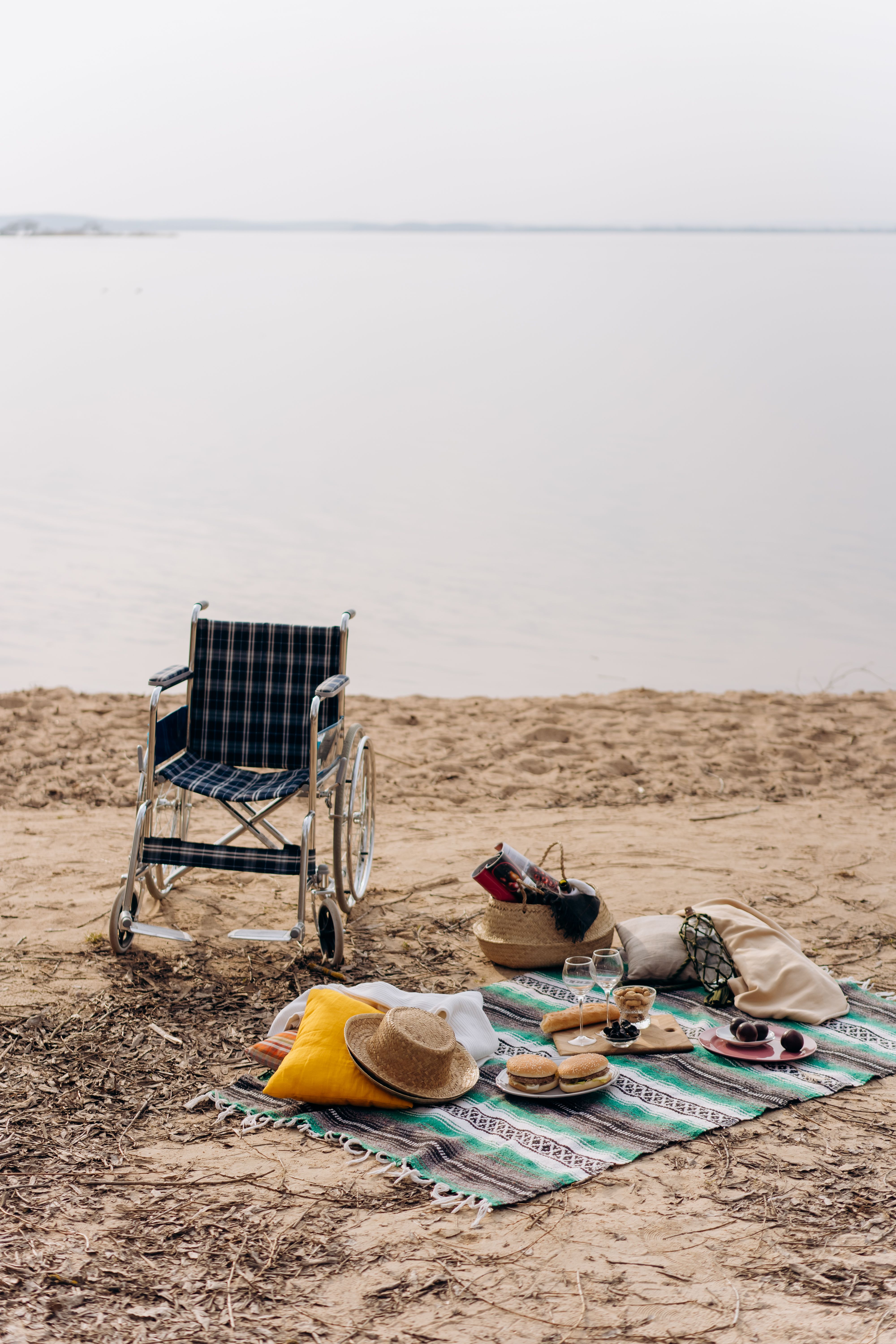 A relaxing beach picnic setup with a wheelchair and essentials by the calm water, evoking accessibility and leisure.