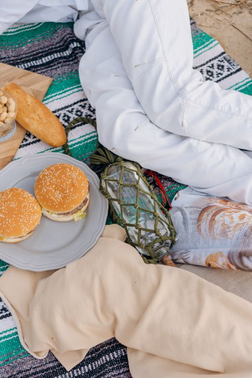 Free A cozy beach picnic with hamburgers on a blanket, perfect for a sunny day. Stock Photo
