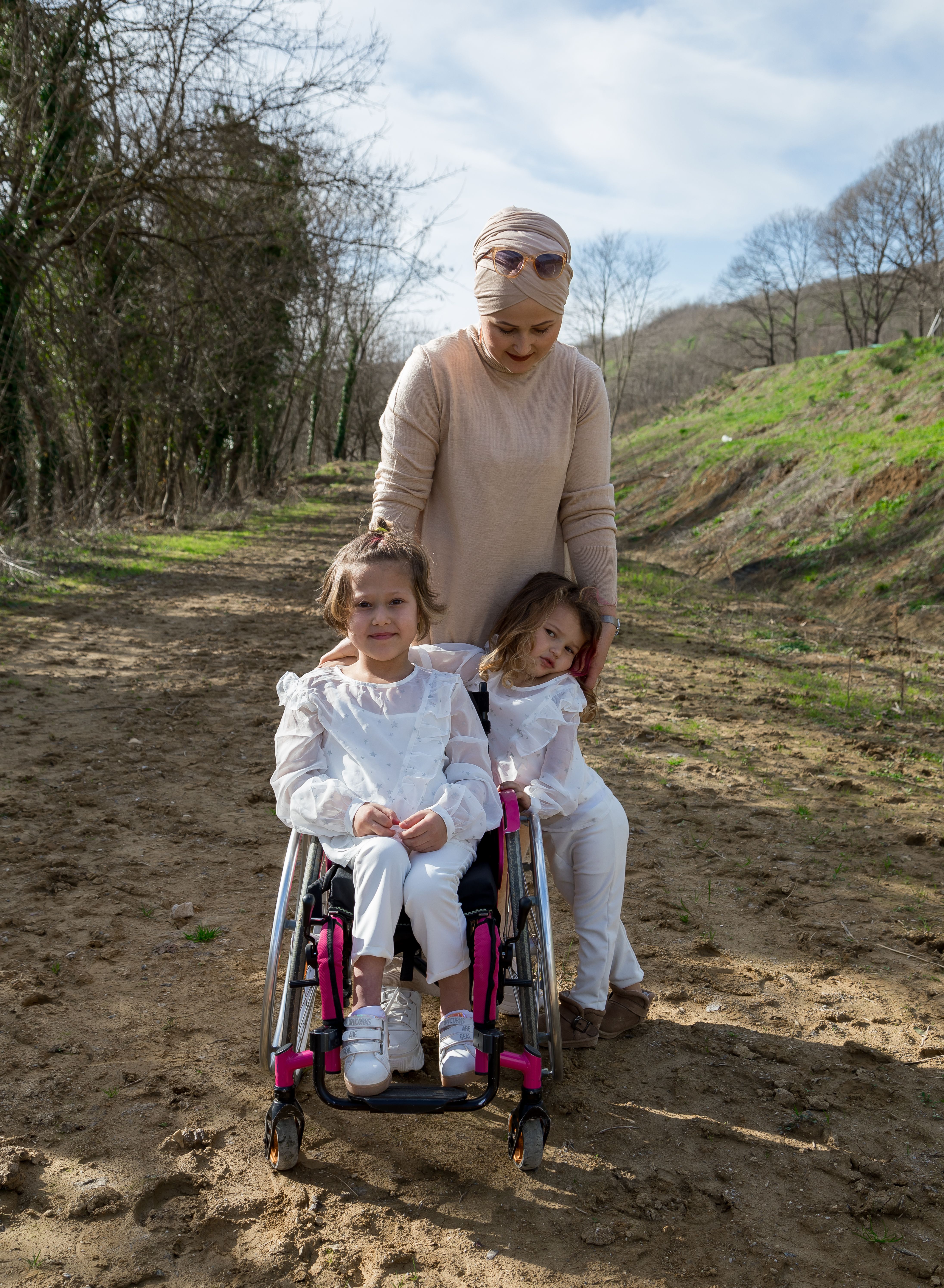 Muslim stylish mother in beige headscarf and hijab with adorable daughters in park with leafless trees
