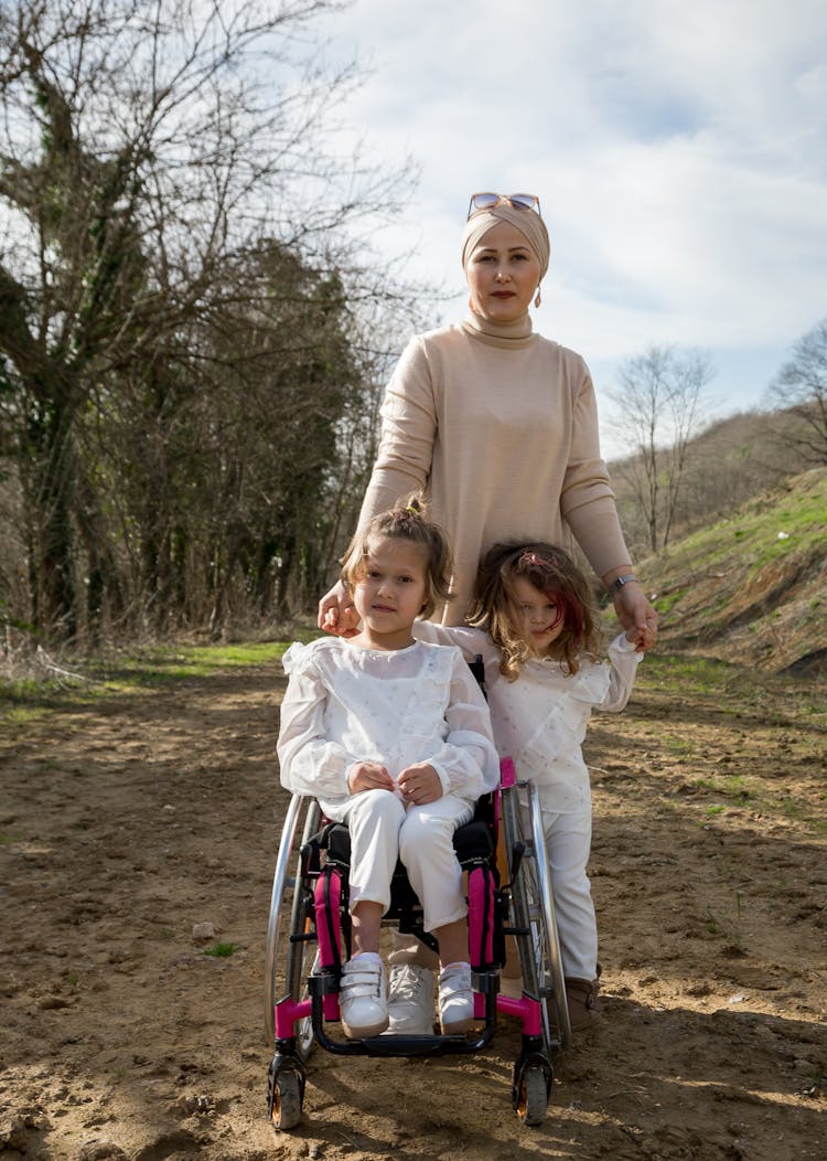 Muslim Mother With Daughter Using Wheelchair Near Happy Girl