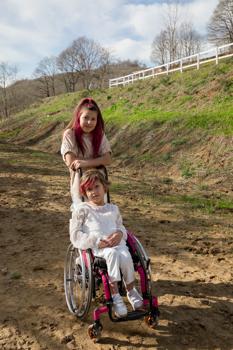 Happy Teenage Girl Near Sister In Wheelchair