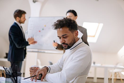 Business man in white attire reviews documents during a collaborative office meeting.