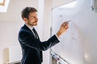 Man in Blue Suit Jacket Writing on White Board