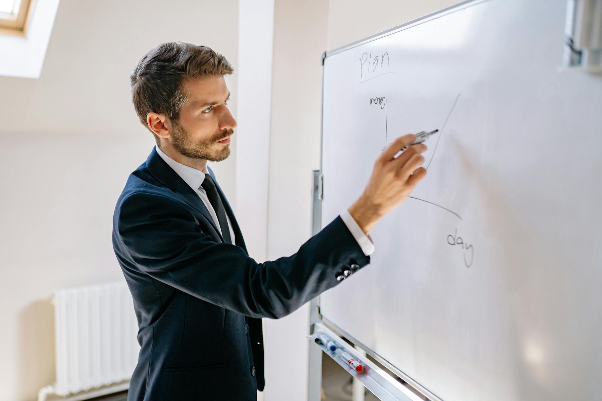 Executive in suit writing on whiteboard, explaining business graph.