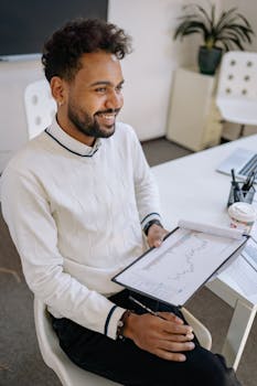Confident businessman reviews financial data on clipboard, smiling in modern office setting.