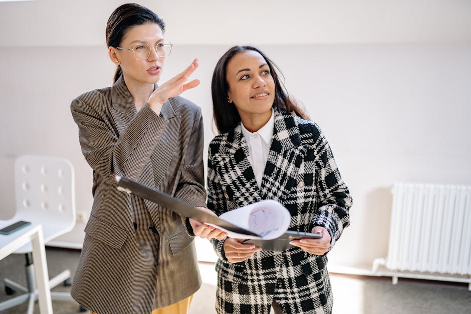 Two businesswomen in stylish suits discuss documents in a modern office setting.