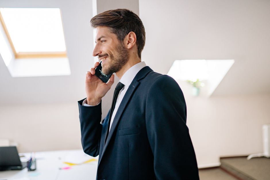 Empresário sorridente em um terno fazendo uma ligação dentro de um ambiente de escritório moderno.