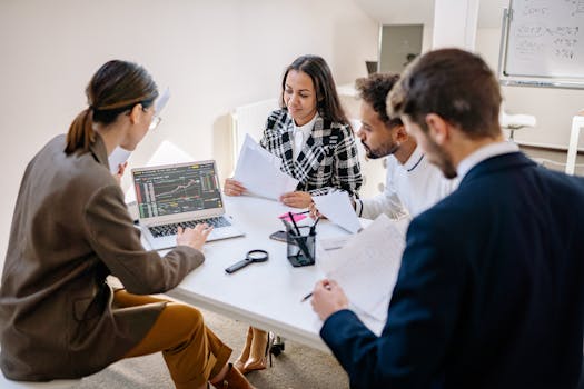 A team of diverse professionals collaborating and analyzing data on a laptop in an office meeting.