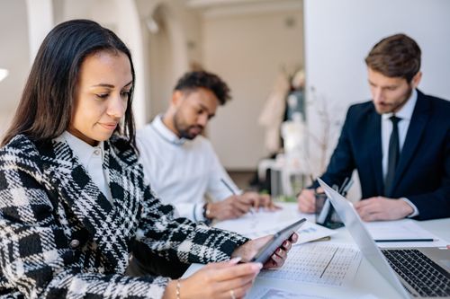 Free Professionals collaborating in a modern office, focusing on a tablet and taking notes. Stock Photo