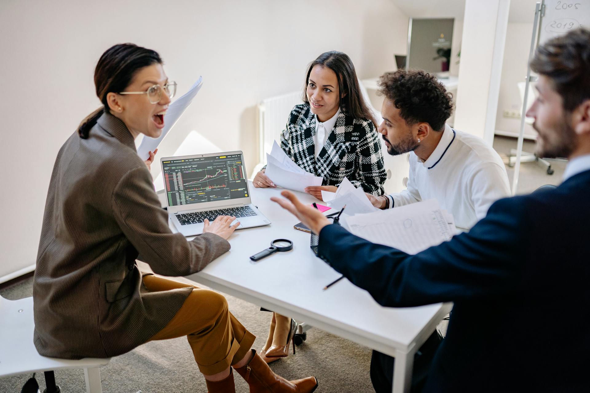 A diverse group of young professionals discussing finances using a laptop in an office setting.