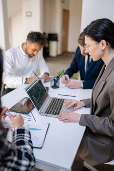 A group of professionals collaborating at a desk with laptops and paperwork.