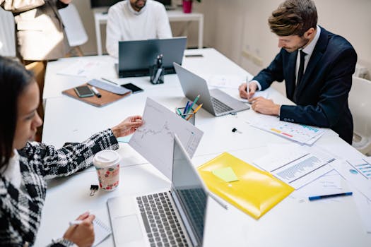 Professionals collaborating in a modern office with laptops and documents, focusing on teamwork.