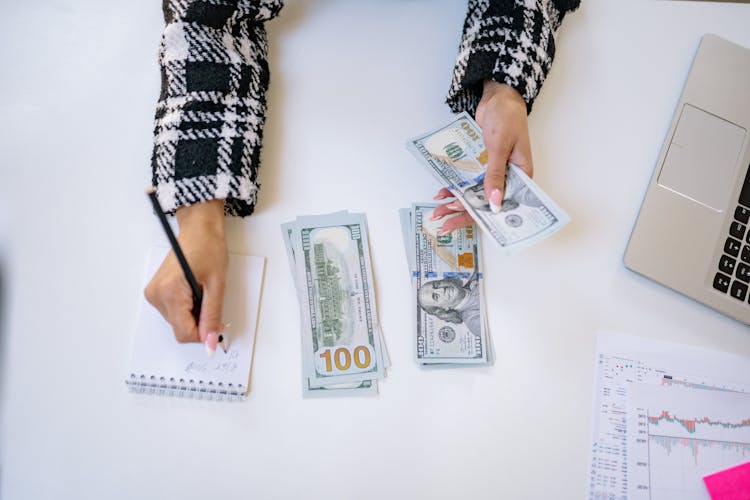 A Person Taking Notes While Counting Money