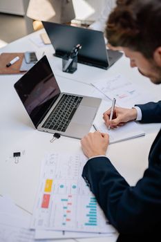 Business professional taking notes with a laptop and documents on a desk. Modern workspace concept.