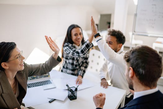 A diverse group of colleagues celebrating success in a bright office setting with high fives.