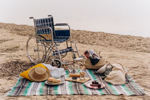 A beachside picnic featuring a wheelchair, food, and blanket on the sand.