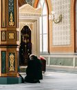 A Man in Black Coat Kneeling in a Mosque