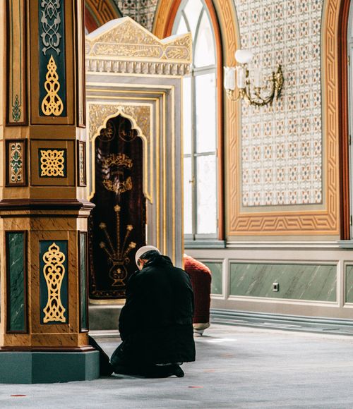 Free A man kneeling and praying inside a beautifully decorated mosque, showcasing intricate Islamic architecture. Stock Photo