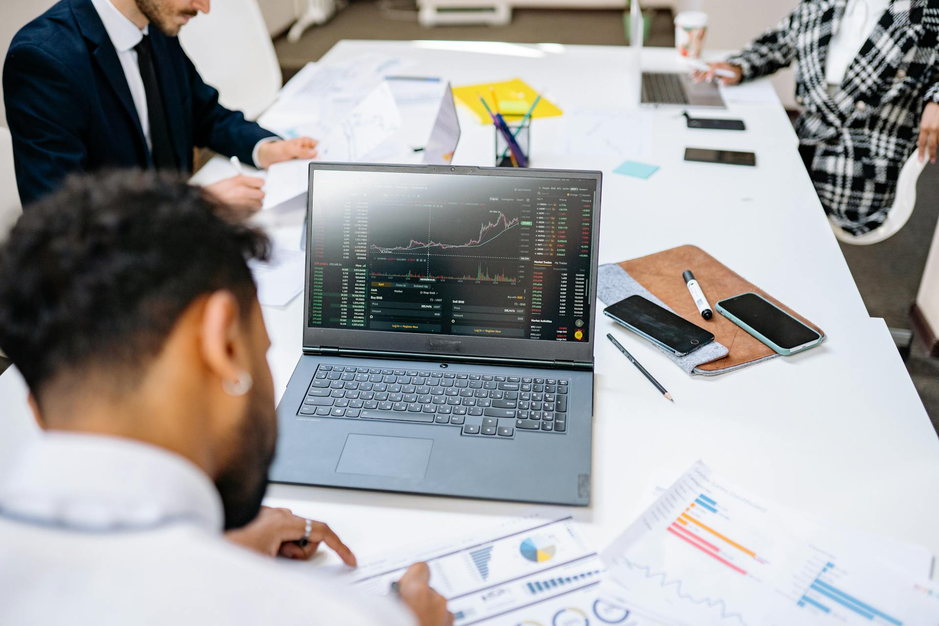 Team collaborating in an office setting, discussing financial graphs on a laptop screen.