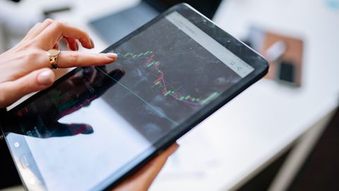 Close-up of a woman using a tablet to analyze stock market graphs.