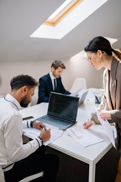 Free Three coworkers collaborate around a laptop in a bright, modern office setting. Stock Photo
