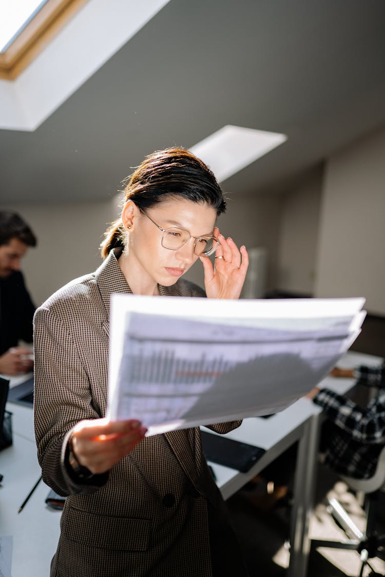 Woman Holding Her Eyeglasses While Looking At The Papers 