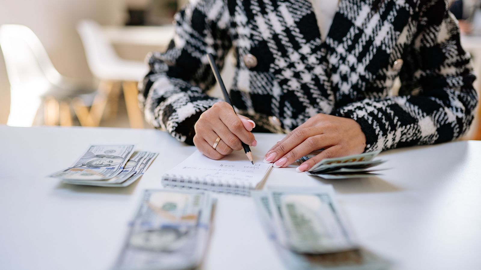 A woman writing in a notepad beside cash on a white table