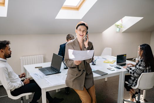Diverse business team collaborating in a bright modern office setting, using laptops and smartphones.