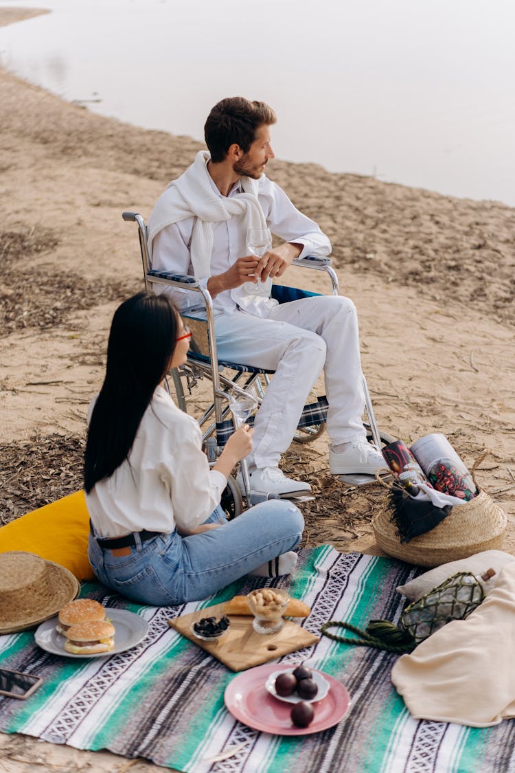 Man On Wheelchair Beside A Woman Sitting On Picnic Blanket