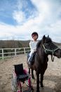 Smiling girl on black pony with wheelchair near
