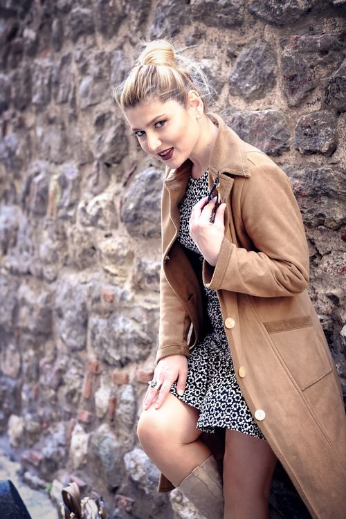 Free Fashionable woman in a brown coat leaning on a stone wall, capturing modern style. Stock Photo