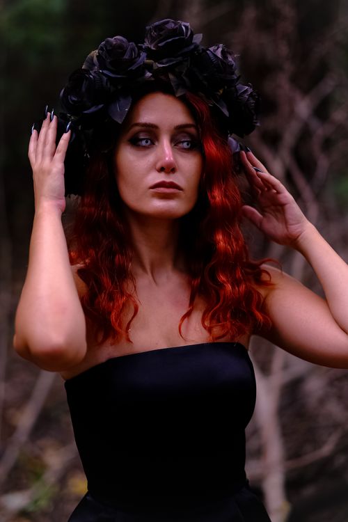 Free Striking portrait of a woman with red hair and a dark floral headdress in a natural setting, conveying elegance and mystery. Stock Photo