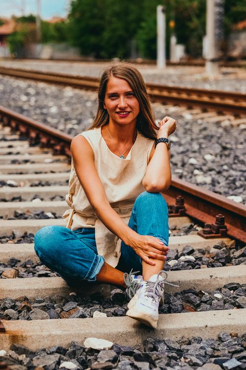 Free Smiling woman in casual attire sits on railway tracks outdoors, embracing summer vibes. Stock Photo