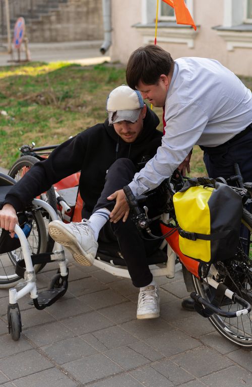 Free A friendly scene of a man helping another adjust a handcycle seat outdoors. Daytime setting. Stock Photo
