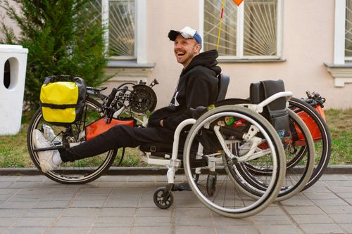 Free A smiling man sitting in a wheelchair next to an adapted bike outdoors. Stock Photo